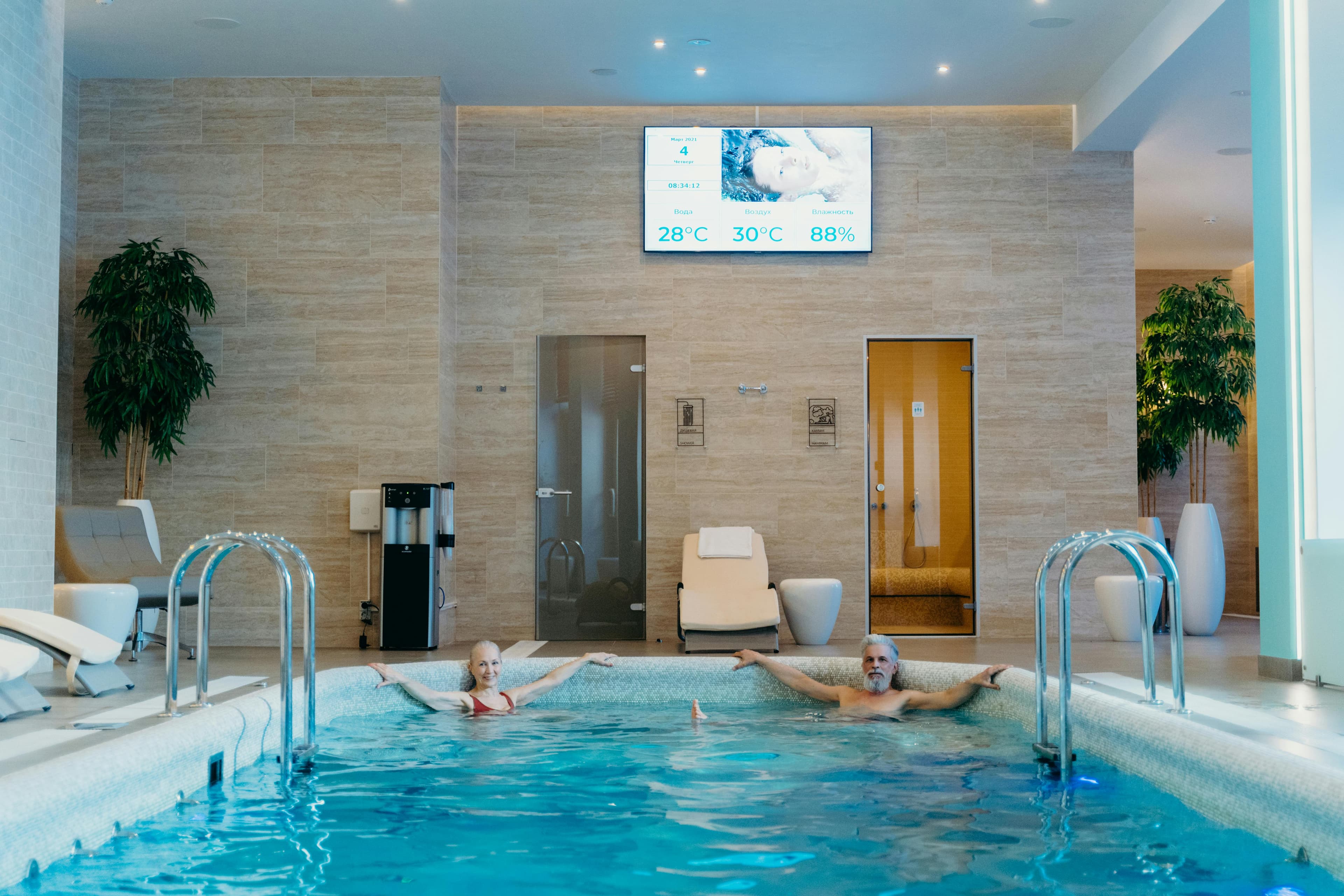 Two adults enjoying leisure time at an indoor swimming pool with spa-like ambiance.